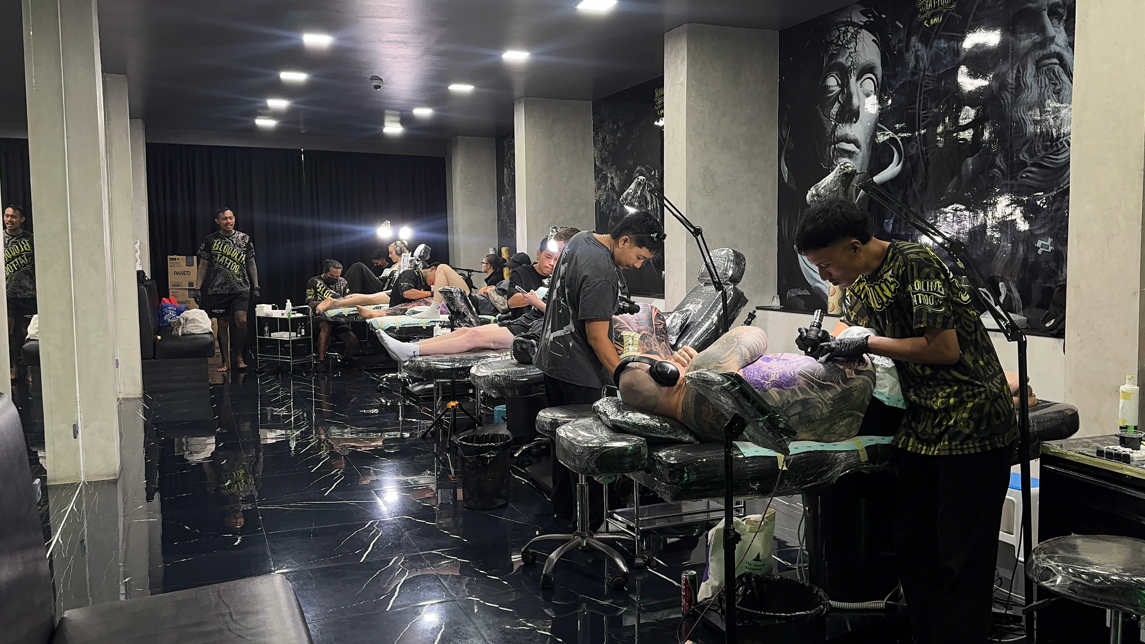 Professional tattoo artists working in the sterile Bloodline Tattoo Bali studio with black and grey realism murals and clinical session standards