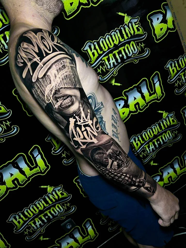 Detailed black and grey Chicano upper arm sleeve tattoo with a blindfolded smoking woman, graffiti script, masked gunman, and checkerboard detail at Bloodline Tattoo Bali.