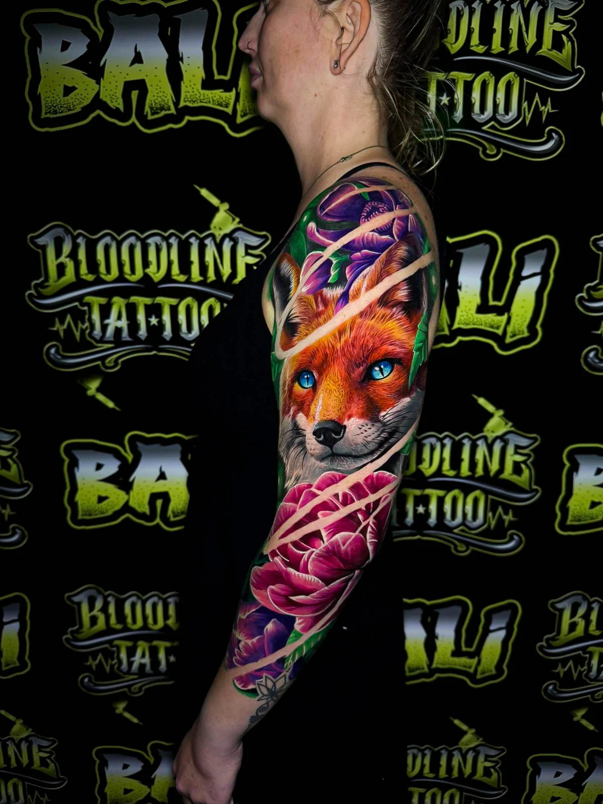 Colour floral arm sleeve tattoo featuring a vivid fox portrait with bright blue eyes, purple blossoms, and pink peonies at Bloodline Tattoo Bali.