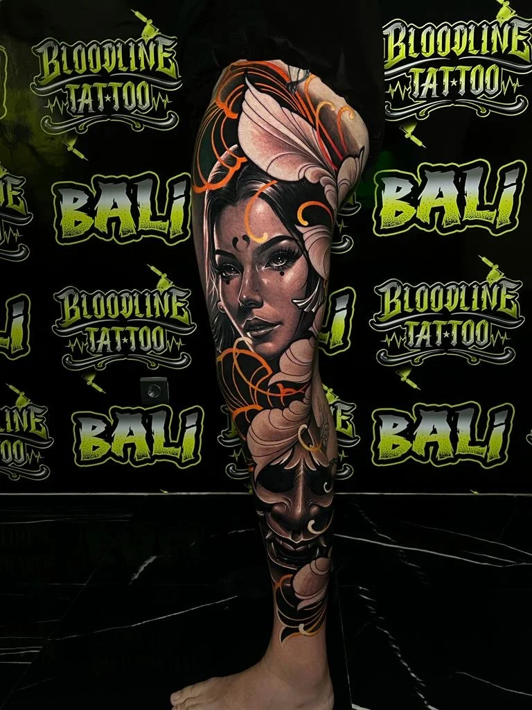 Colour neo-traditional leg tattoo of a glamorous female portrait framed by large cream petals and warm orange decorative lines at Bloodline Tattoo Bali.