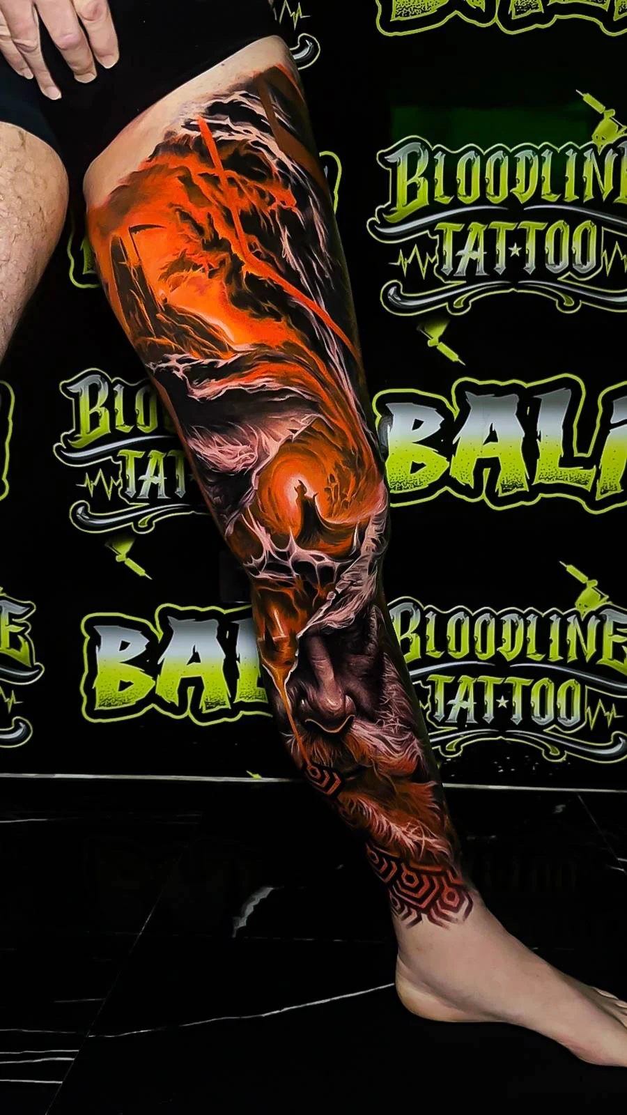Colour dark fantasy leg tattoo with an orange storm vortex, twisted trees, and a wolf portrait emerging through the lower composition at Bloodline Tattoo Bali.