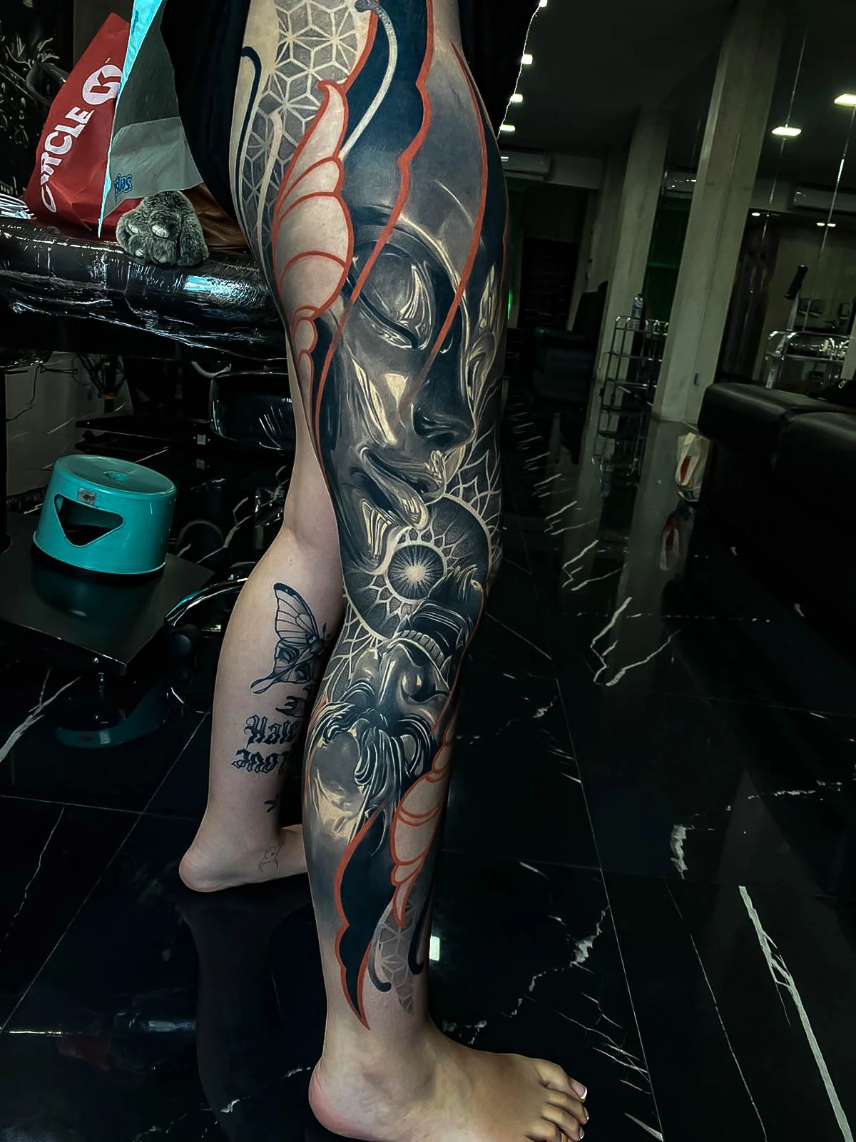 Healed leg sleeve with a female face, butterfly wing, sacred-geometry accents, and red contour highlights, holding smooth healed contrast at Bloodline Tattoo Bali.