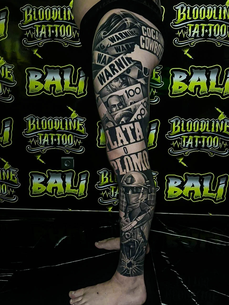 Healed collage leg sleeve with money, bold lettering, warning tape, and biker imagery, showing strong healed contrast and sharp edge definition at Bloodline Tattoo Bali.