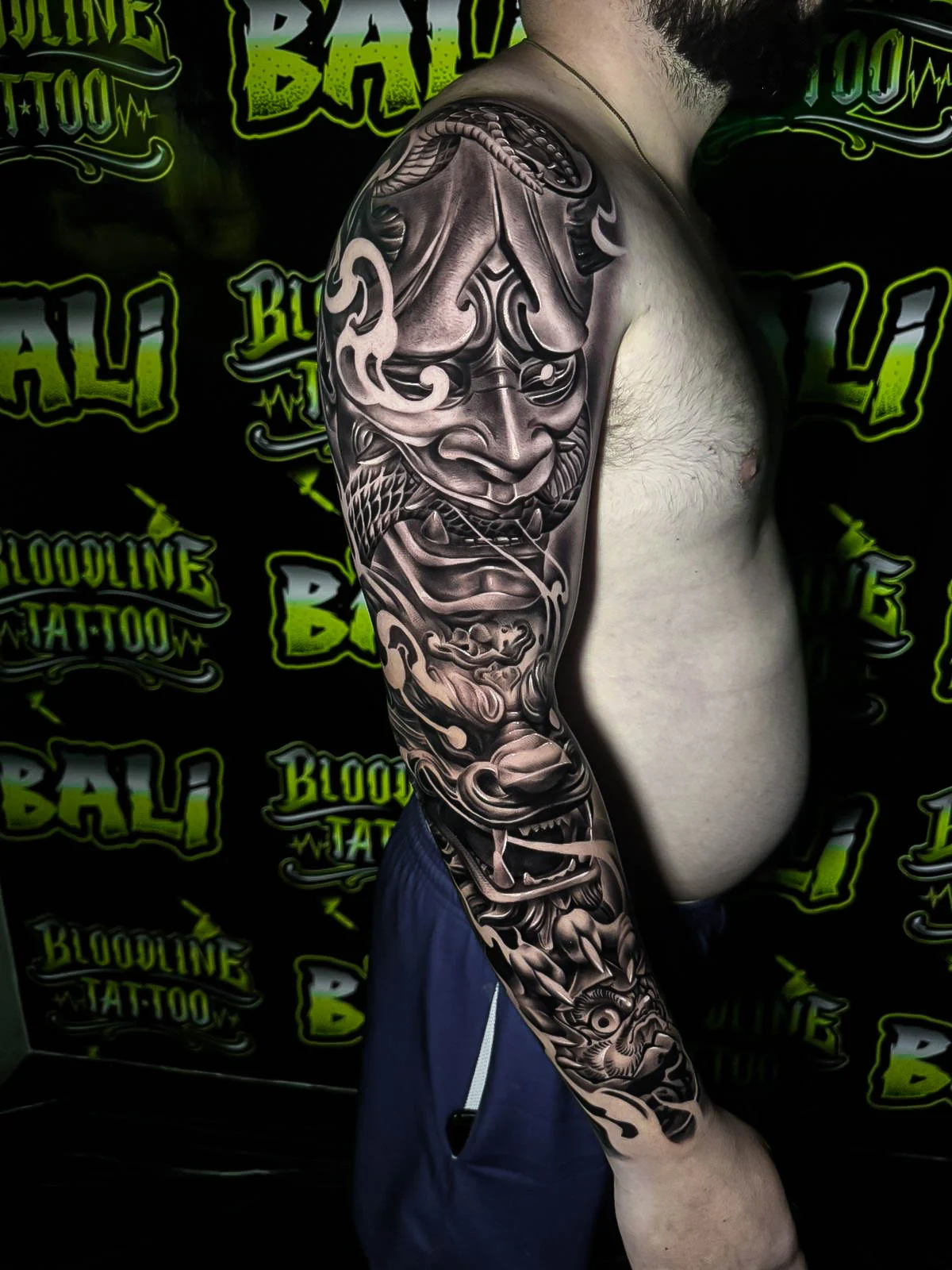 Black and grey Japanese full sleeve with a Hannya mask, wind bars, wave details, and koi imagery at Bloodline Tattoo Bali.
