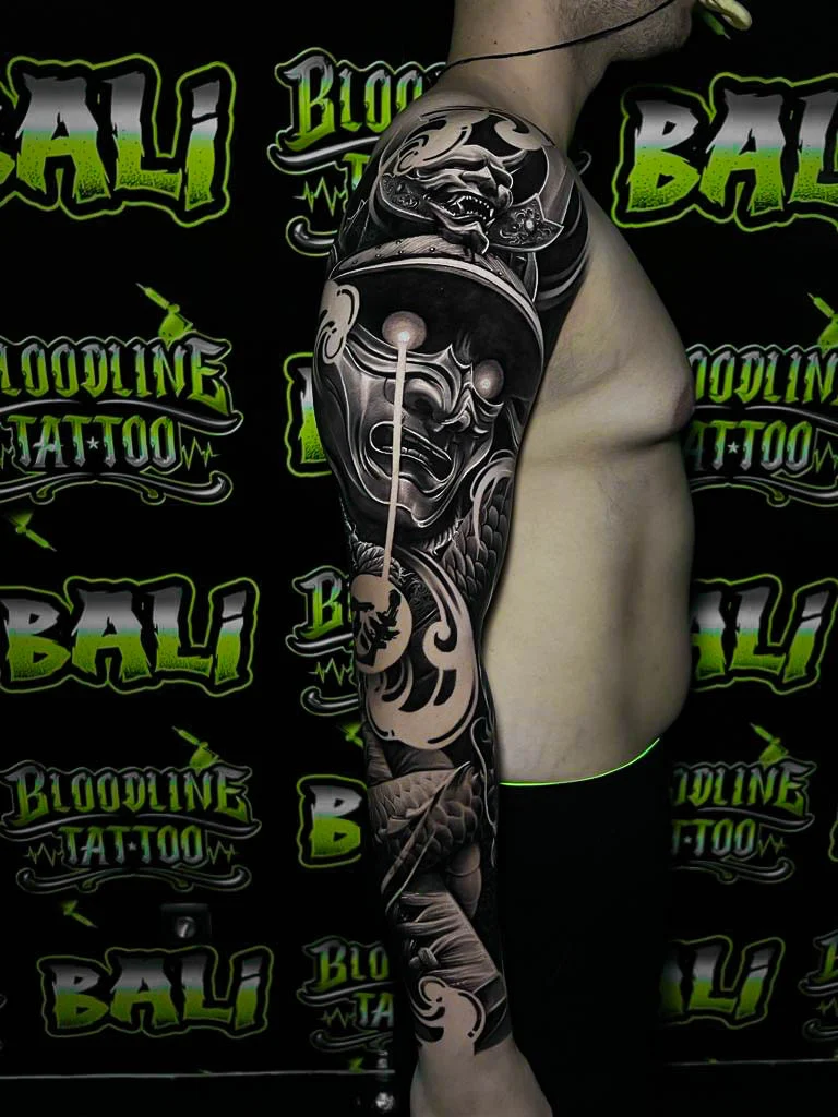 Black and grey Japanese half sleeve with a Hannya mask, snake, hanging lantern, and wave smoke at Bloodline Tattoo Bali.