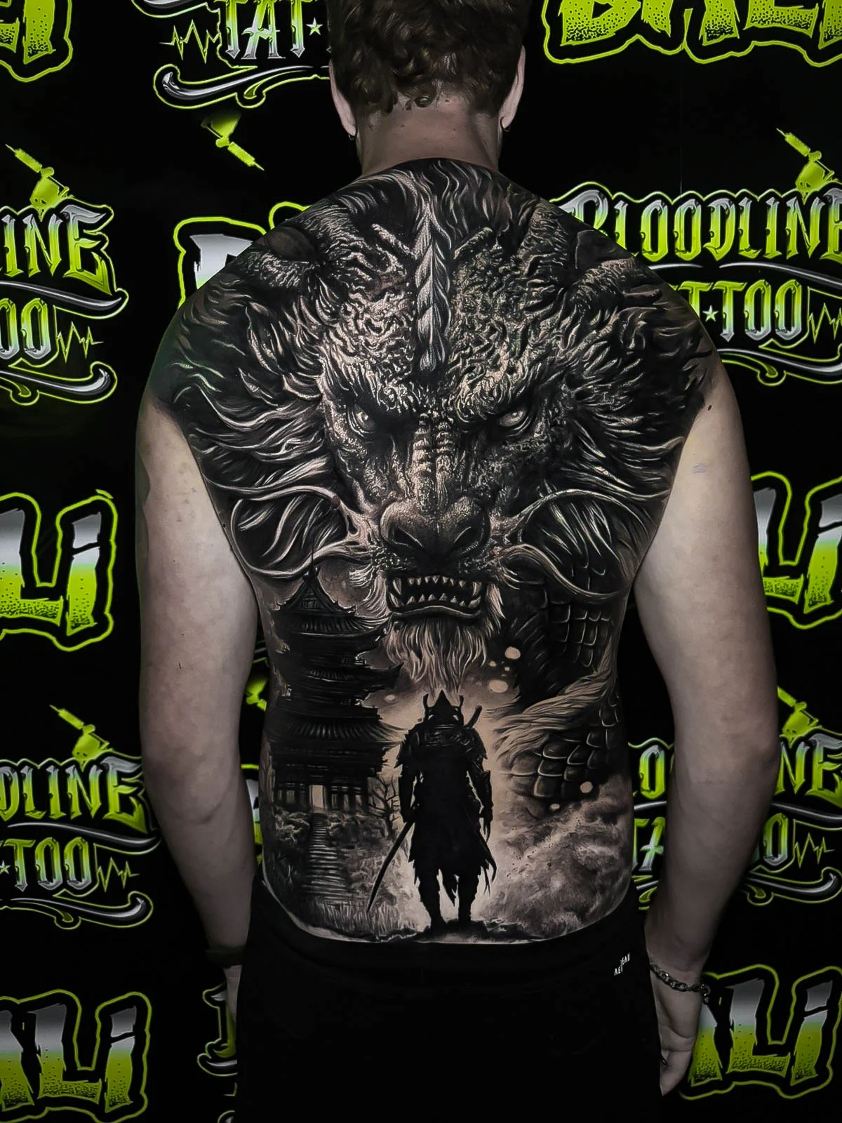 Black and grey Japanese full back piece with a dragon face, pagoda, and lone samurai silhouette at Bloodline Tattoo Bali.