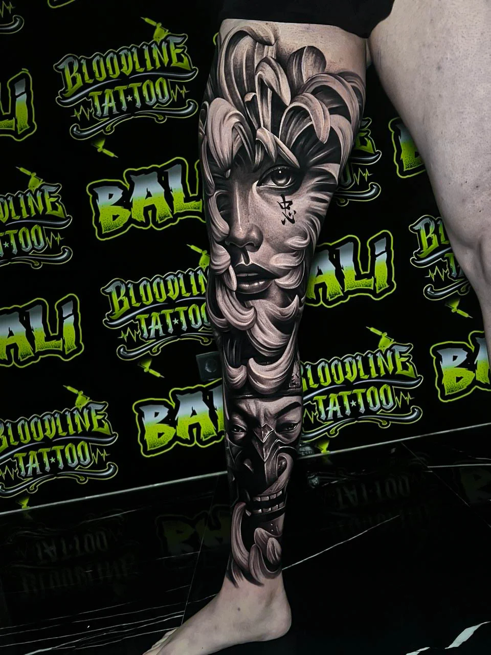 Black and grey Japanese leg sleeve with a geisha portrait, flowing chrysanthemum petals, and an oni mask at Bloodline Tattoo Bali.