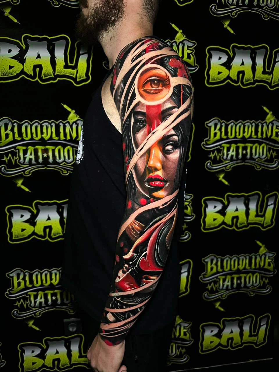 Japanese-inspired colour full sleeve with a bandaged female face, all-seeing eye, and red-black abstract ribbons at Bloodline Tattoo Bali.