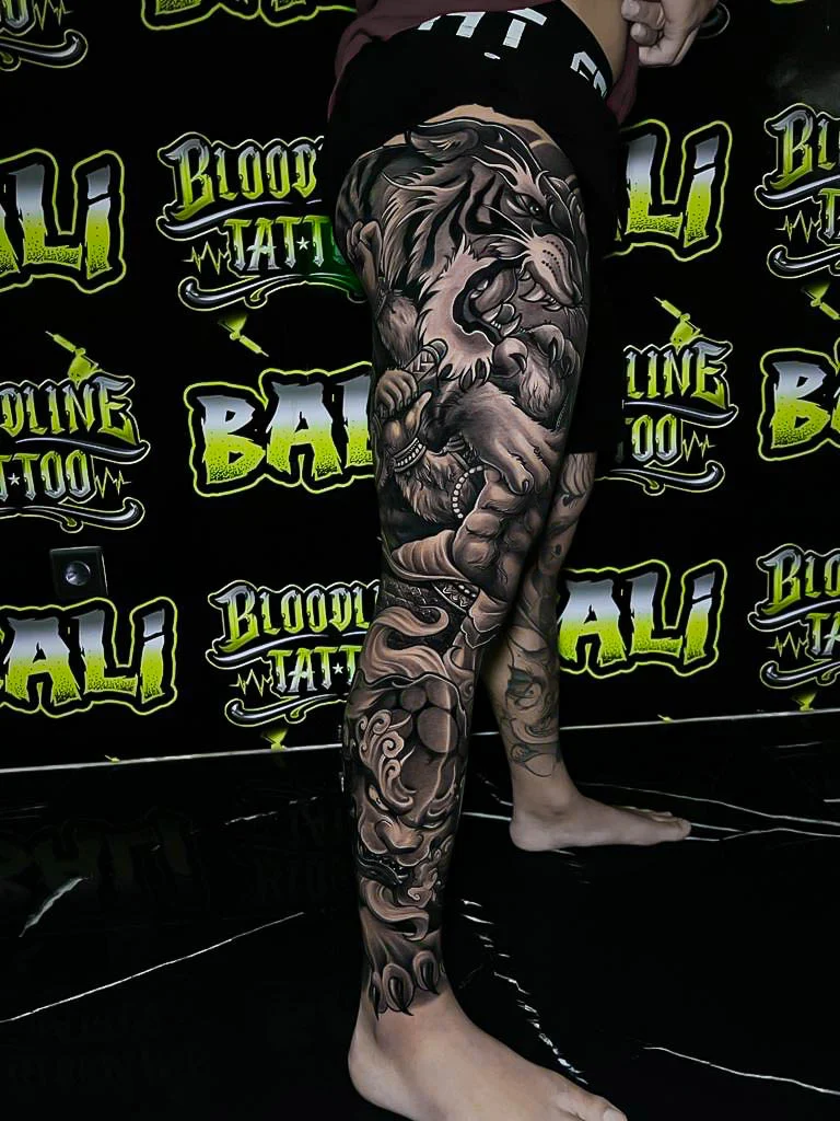 Black and grey Japanese full leg sleeve with a guardian beast, muscular figure, and crashing waves at Bloodline Tattoo Bali.