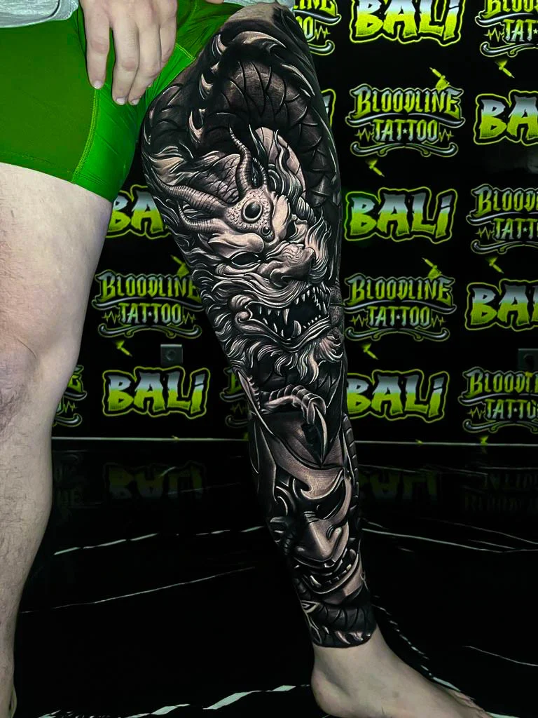 Black and grey Japanese full leg sleeve with a horned yokai skull, snarling beast face, and Hannya mask at Bloodline Tattoo Bali.