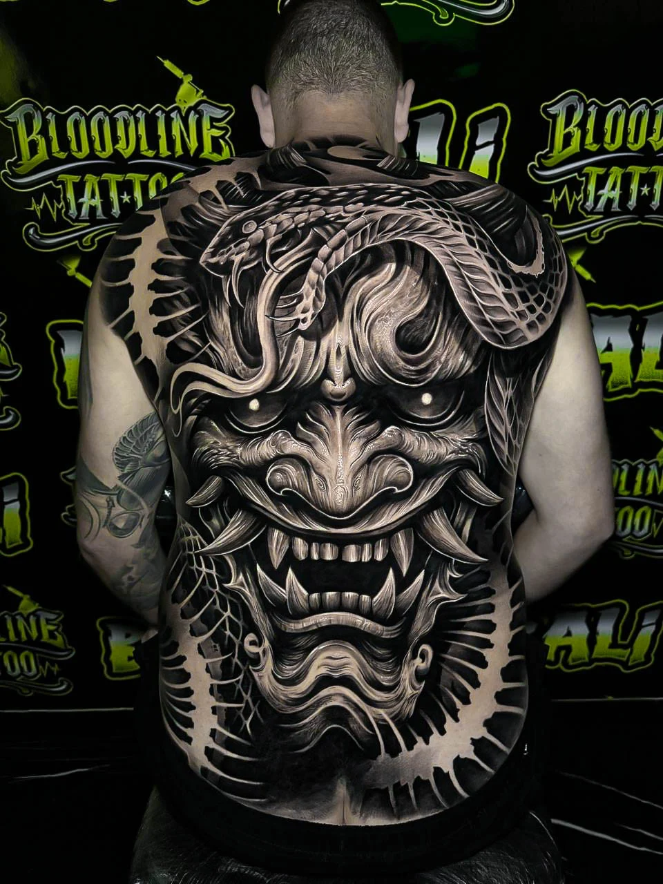 Black and grey Japanese full back piece with a giant Hannya mask, coiled snake, and rib-like negative space at Bloodline Tattoo Bali.