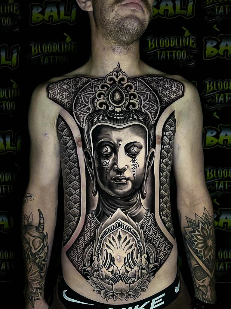 Full torso Buddha composition with Flower of Life shoulders, ornamental crown work, and dot-shaded sacred geometry framed down the sternum at Bloodline Tattoo Bali.