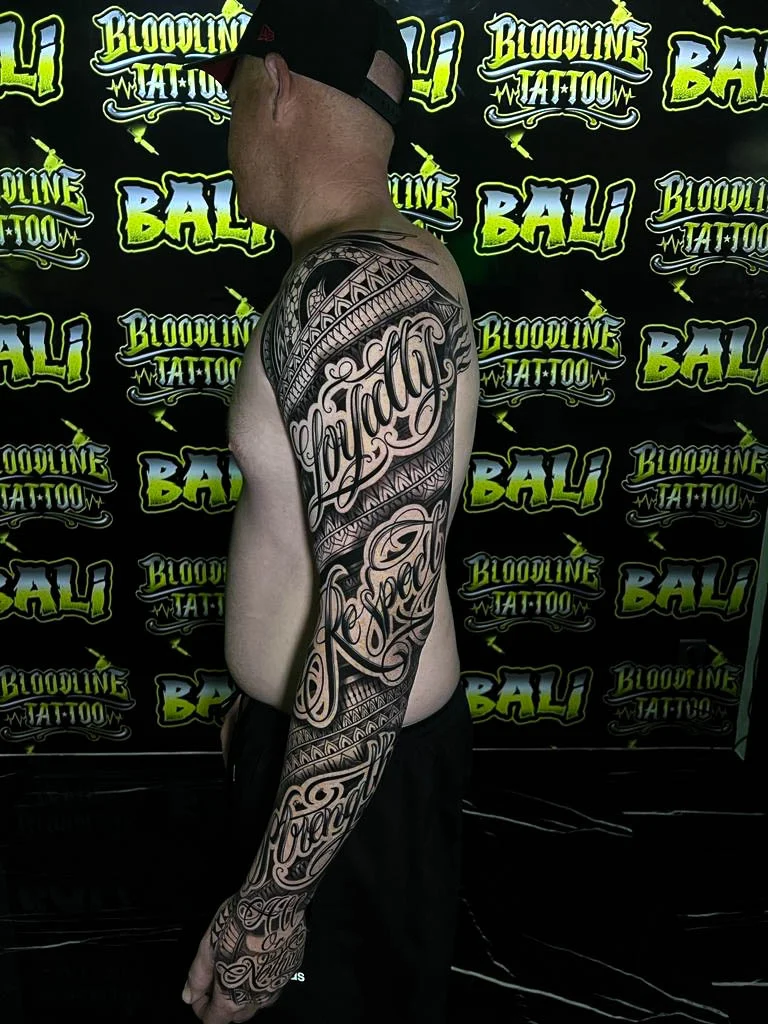 Polynesian-style script sleeve with ornamental tribal bands, interlocking triangle motifs, and smooth blackwork tapering down the forearm at Bloodline Tattoo Bali.