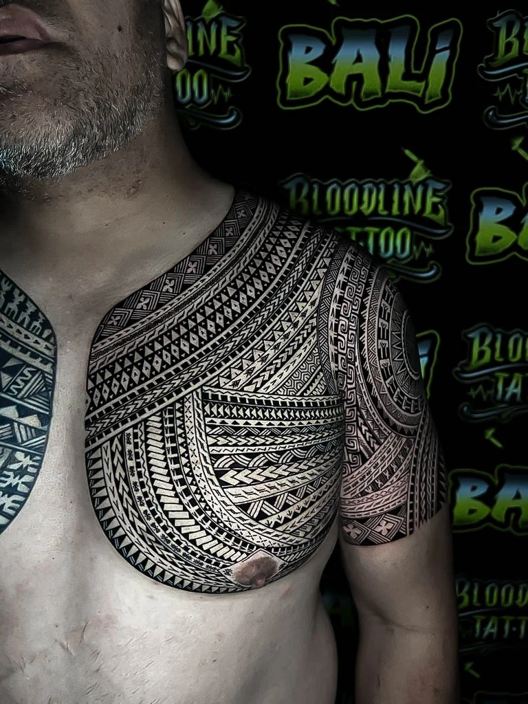 Polynesian chest and shoulder coverage with flowing tribal bands, Greek-key details, and precise blackwork line rhythm across the pec and deltoid at Bloodline Tattoo Bali.