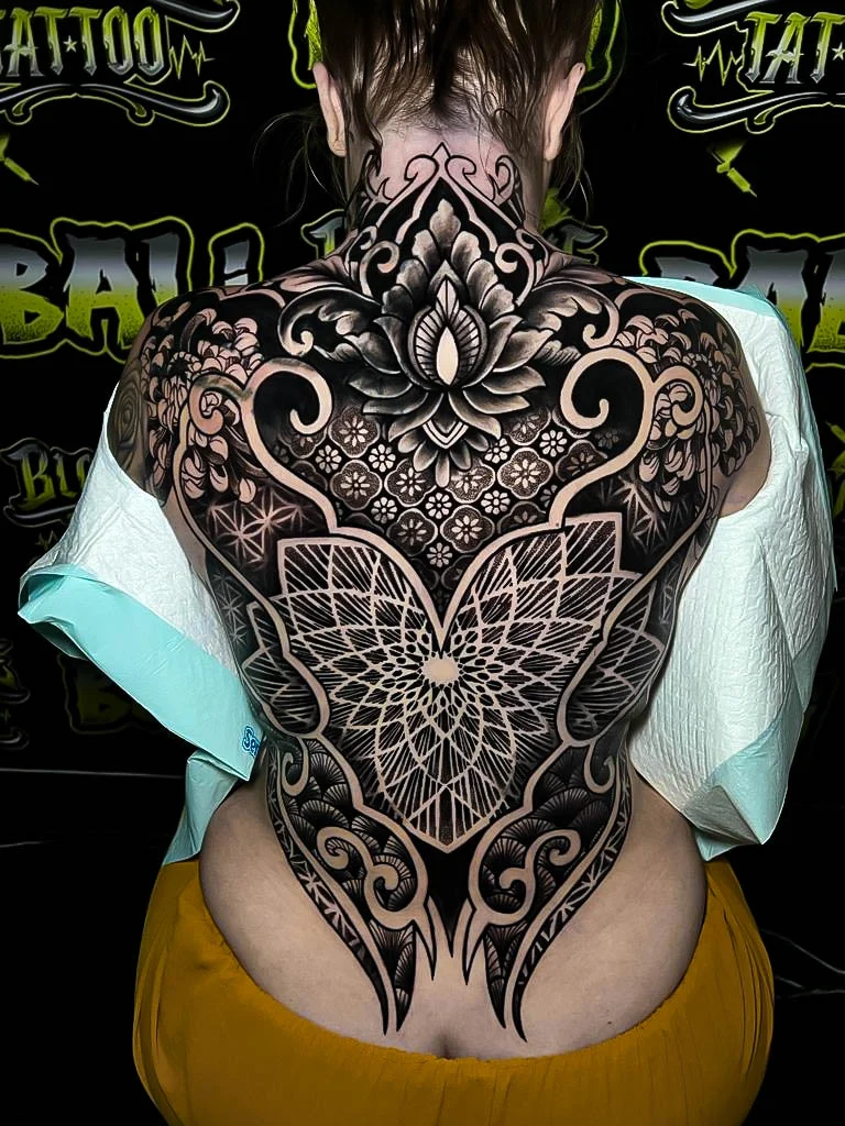 Ornamental backpiece with a lotus neck crown, floral scrollwork, star-grid geometry, and heavy blackwork shaping through the mid-back at Bloodline Tattoo Bali.