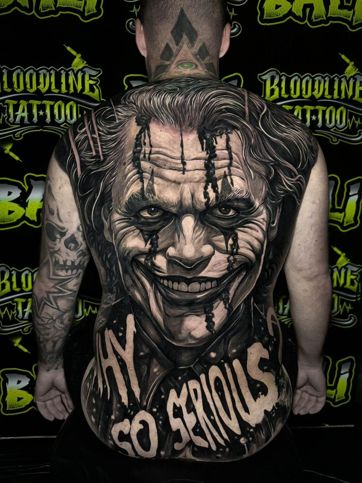 Black and grey portrait realism full back tattoo of the Joker with smeared makeup and bold Why So Serious lettering at Bloodline Tattoo Bali.