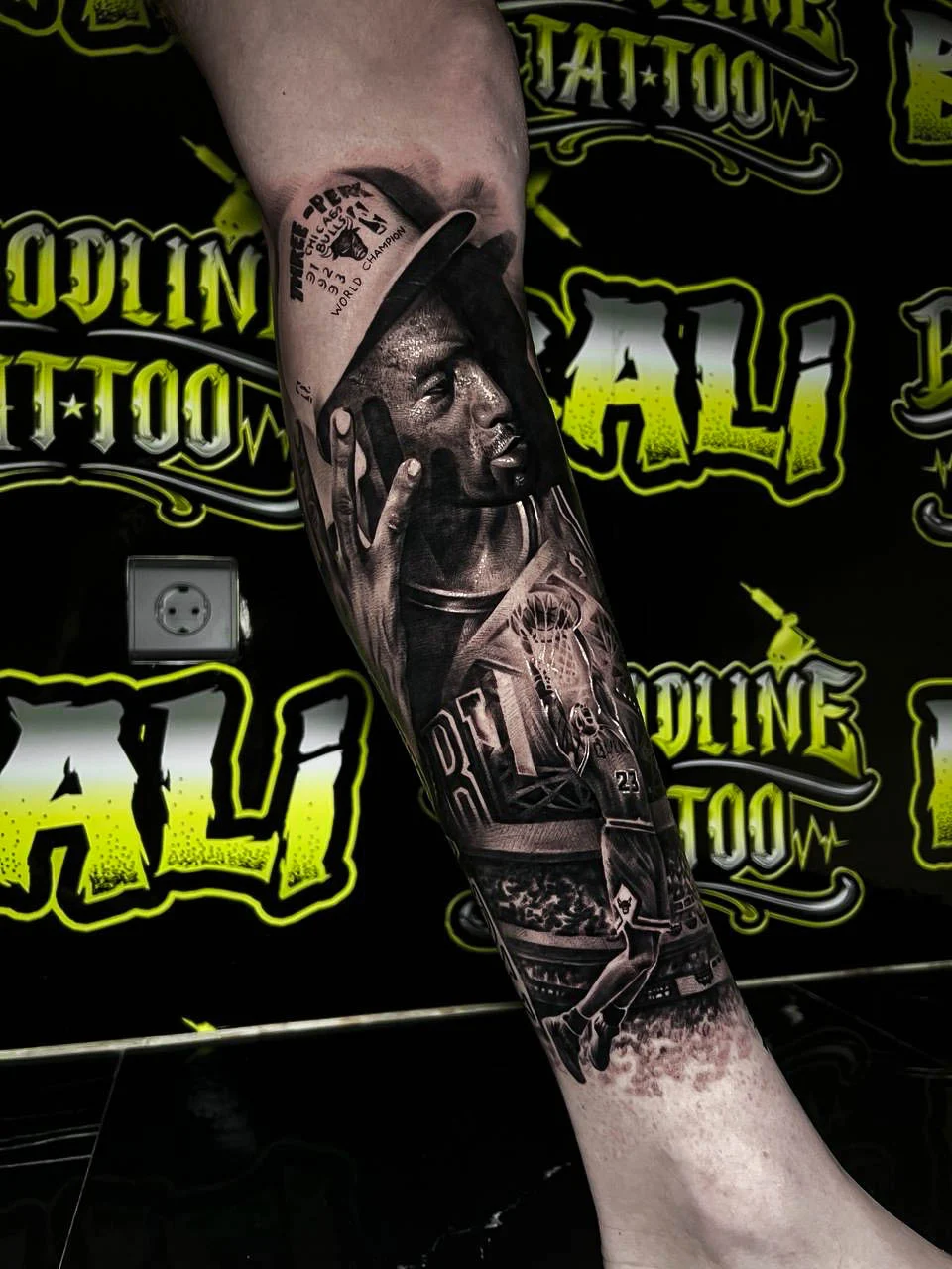 Black and grey portrait realism calf tattoo of Kobe Bryant in profile with jersey number, hoop scene, and championship references at Bloodline Tattoo Bali.
