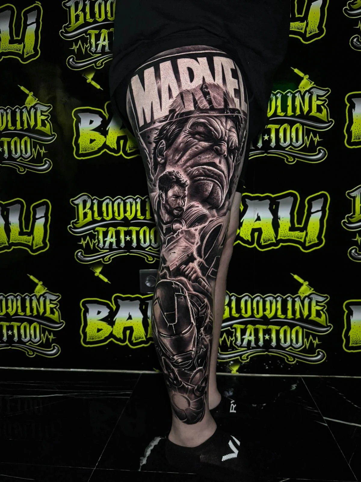 Black and grey portrait realism Marvel leg sleeve tattoo featuring Thanos, Iron Man, and comic-book action scenes at Bloodline Tattoo Bali.