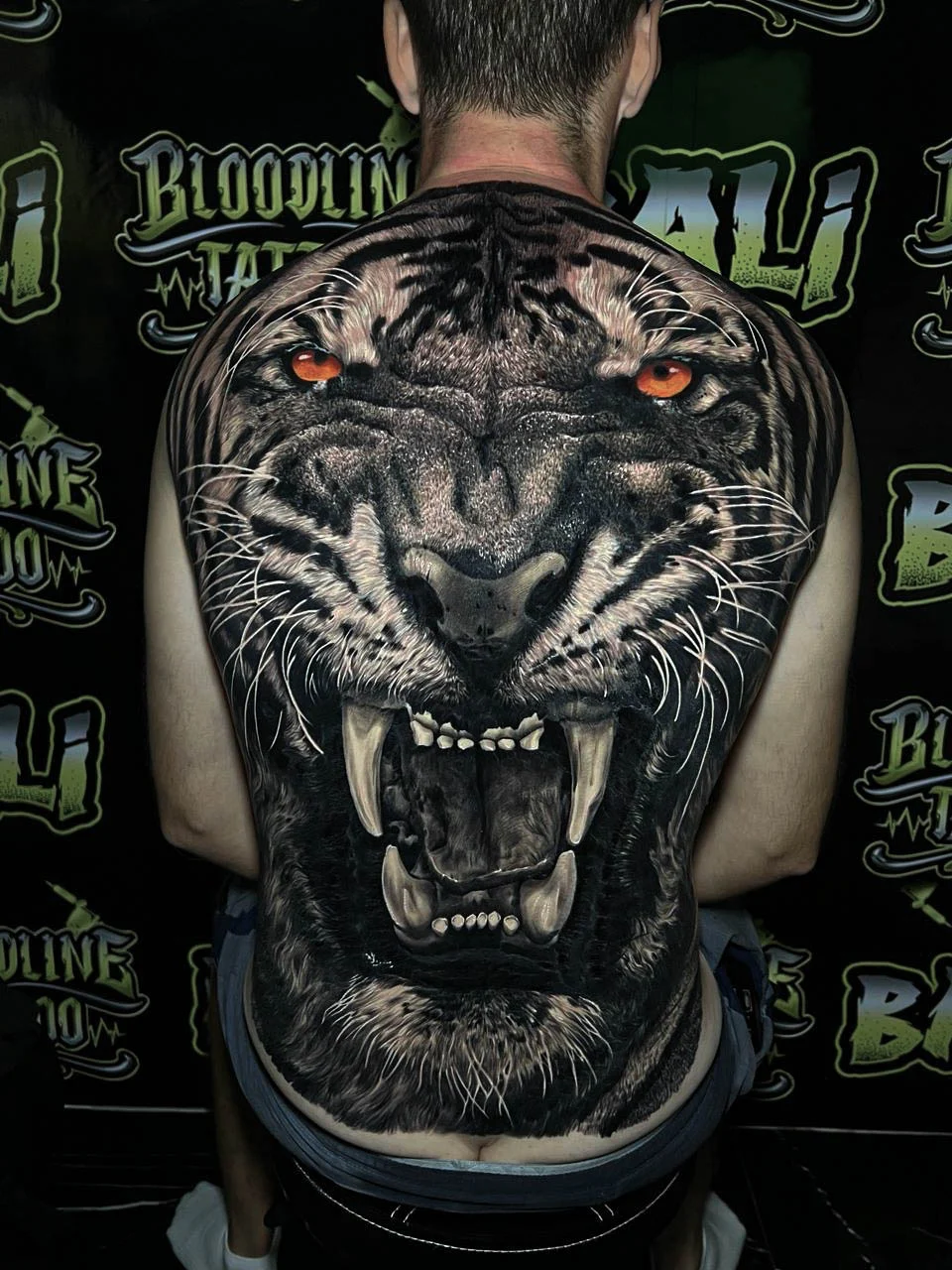 A black and grey realism full back piece of a roaring black panther head with piercing eyes and deep shadowed fur detail, at Bloodline Tattoo Bali.