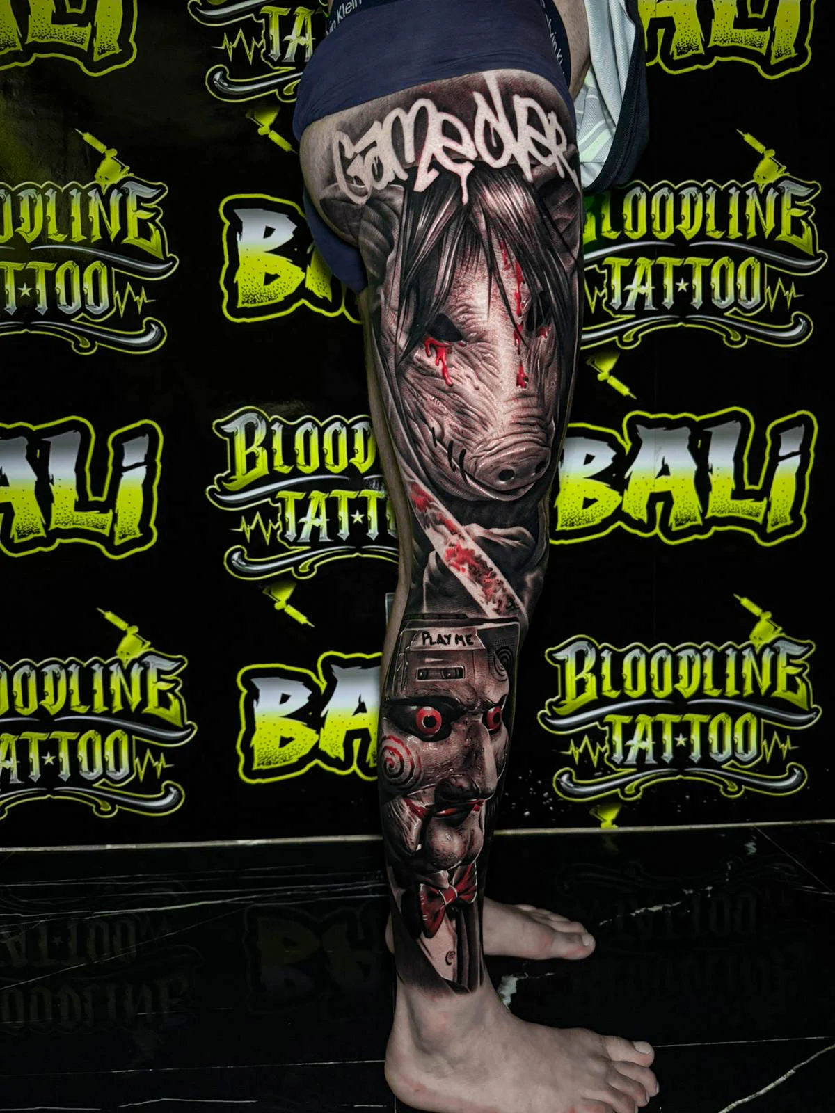 A black and grey realism forearm sleeve of a sinister horror face with scarred skin, deep shadows, and blood-red accent details, at Bloodline Tattoo Bali.