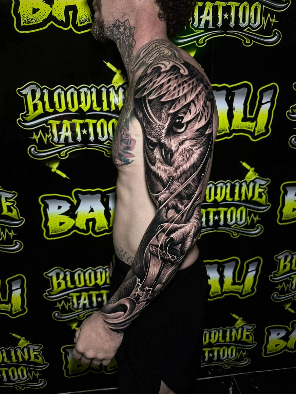A black and grey realism full sleeve with an eagle head, layered roses, and smooth shadow gradients wrapping the upper arm and forearm, at Bloodline Tattoo Bali.