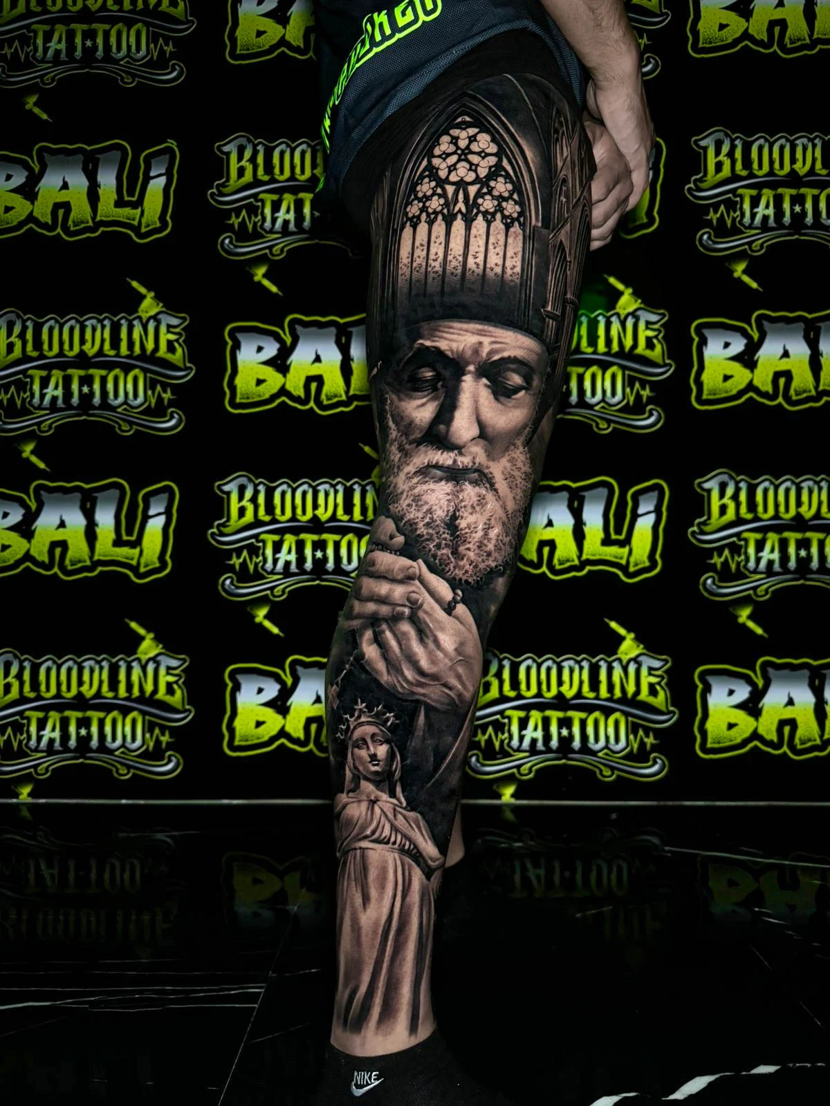 A black and grey realism forearm sleeve of an elderly bishop portrait with weathered facial detail and cathedral-inspired headwear, at Bloodline Tattoo Bali.