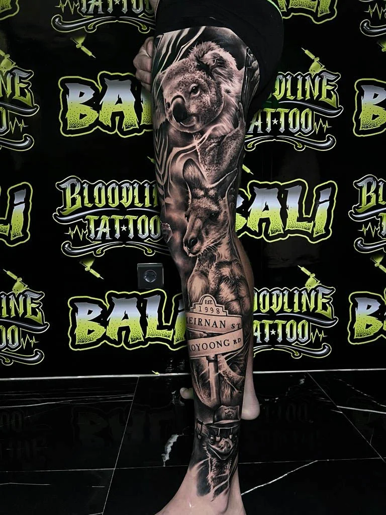 A black and grey realism arm sleeve with a solemn male portrait, script detail, and dark atmospheric shading through the upper arm, at Bloodline Tattoo Bali.